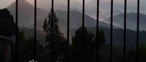 Vista a través de una ventana con barrotes, mostrando un amanecer sobre una cadena de colinas y árboles.