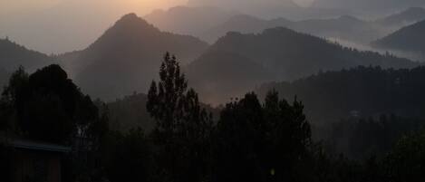 Amanecer sobre un paisaje montañoso con un edificio en primer plano.