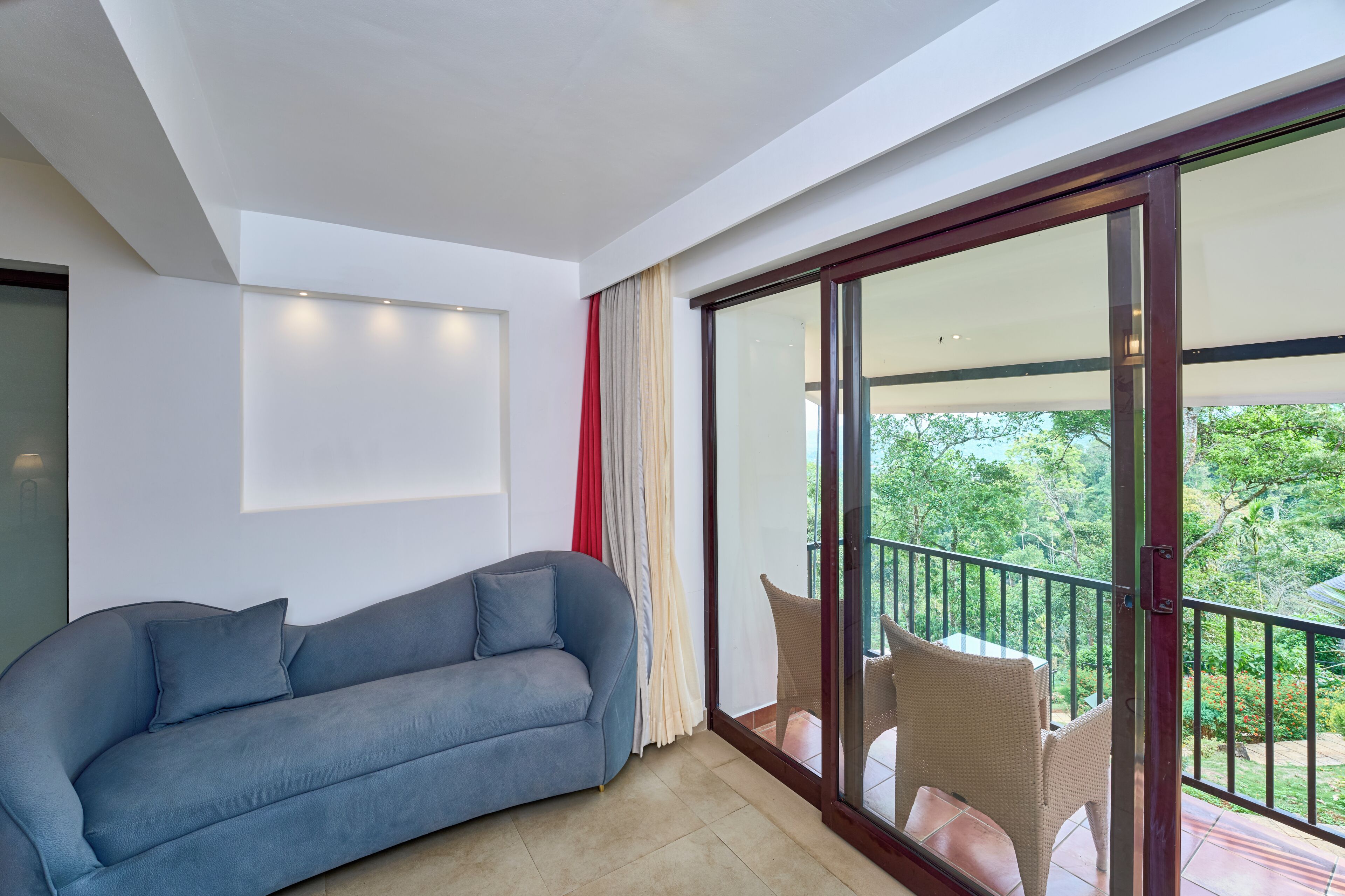 Un salon moderne avec un canapé, une porte-fenêtre coulissante donnant sur un balcon et une vue sur la verdure.
