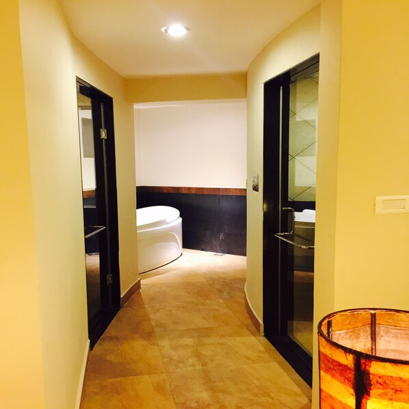 A narrow hallway with a white toilet, a glass-enclosed shower area, and a tiled floor.