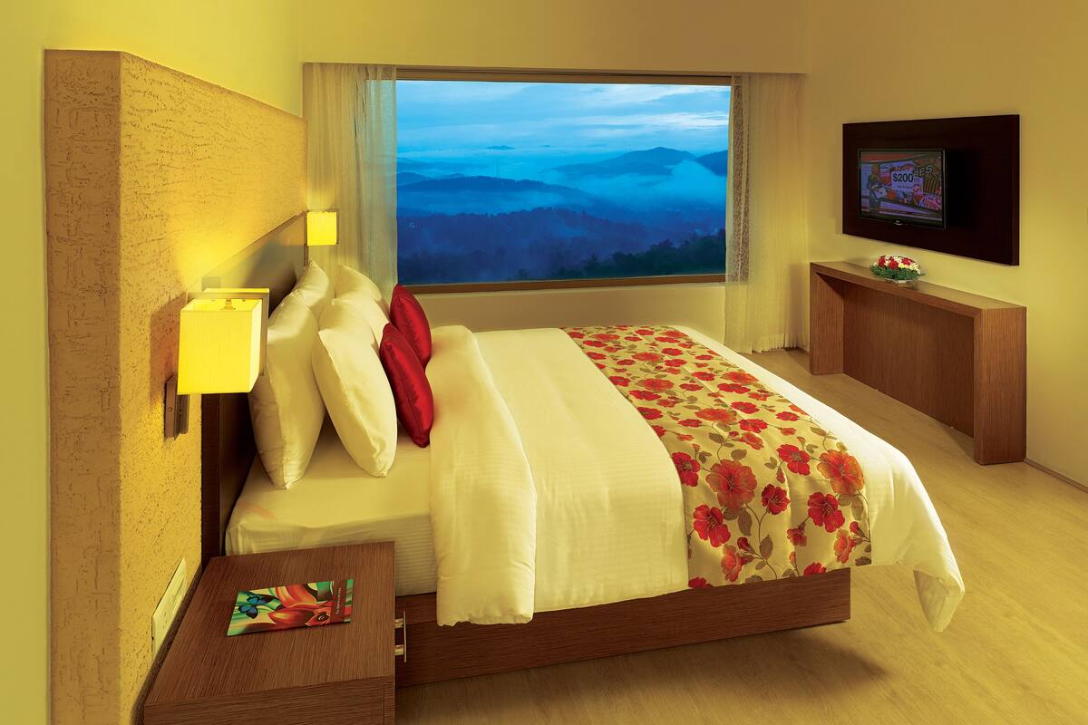 Une chambre d’hôtel avec un lit, une télévision, une table de chevet et une fenêtre donnant sur les montagnes.