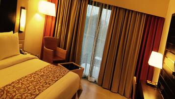 Una habitación de hotel con una cama grande, una silla, un escritorio y un ventanal con cortinas.