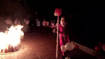 Una persona vestida de rosa sostiene globos en un evento nocturno, con un fuego de fondo.