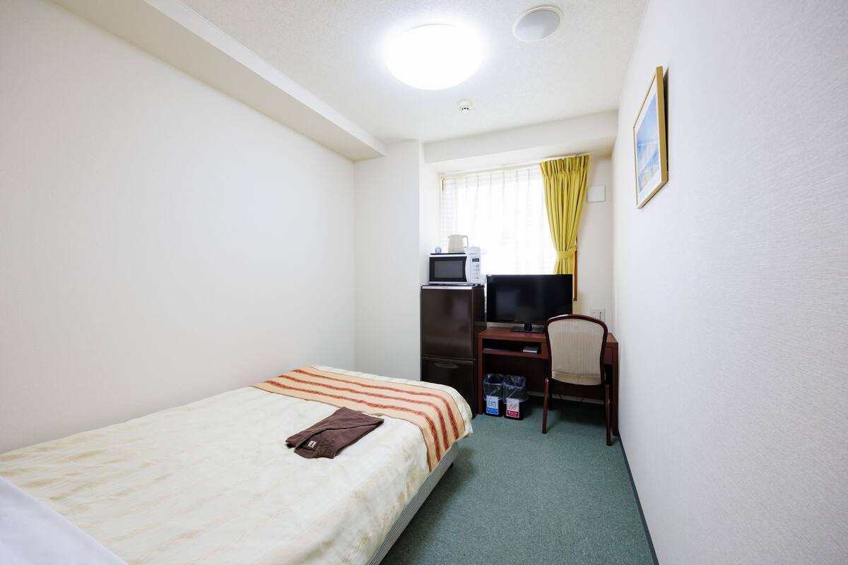 Una habitació d'hotel amb un llit, una taula de treball, una cadira, una televisió i una finestra amb cortines.