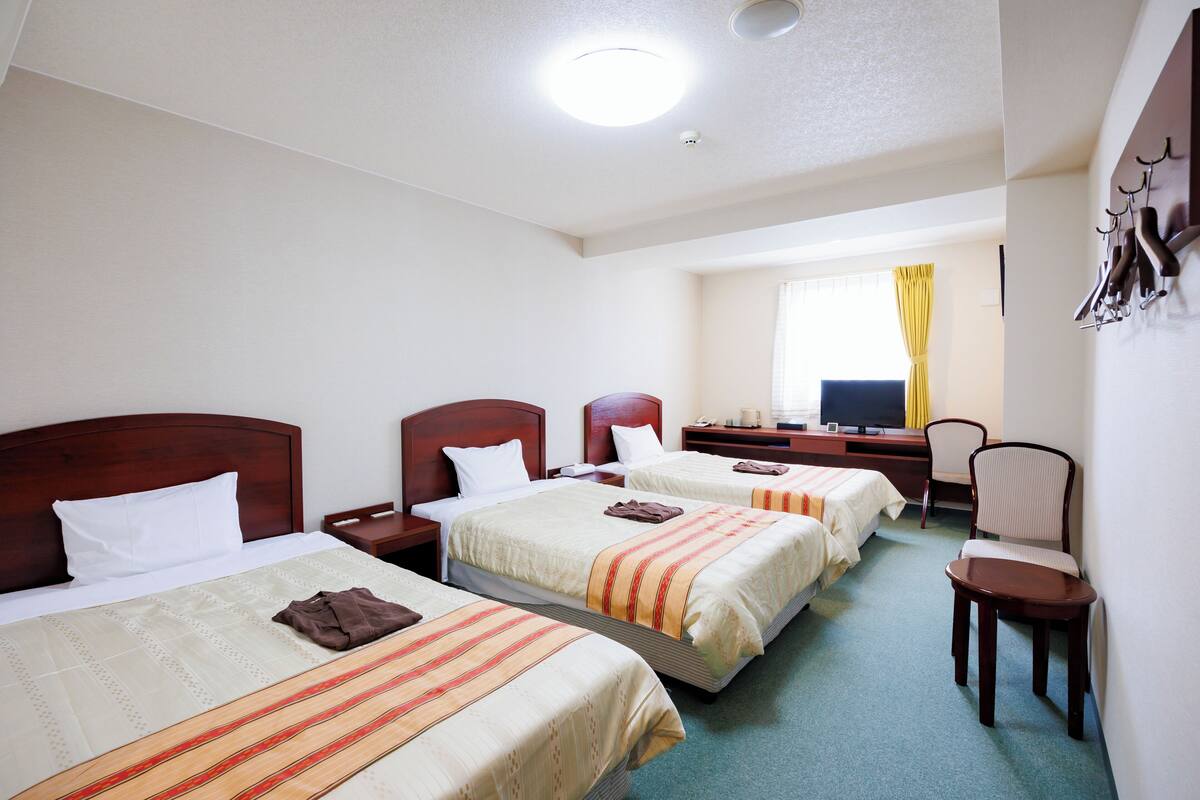 Habitació d'hotel amb tres llits, una taula de treball, una cadira i una televisió.