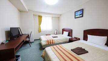 Quarto de hotel com duas camas, uma escrivaninha com computador, uma cadeira e uma janela com cortinas.