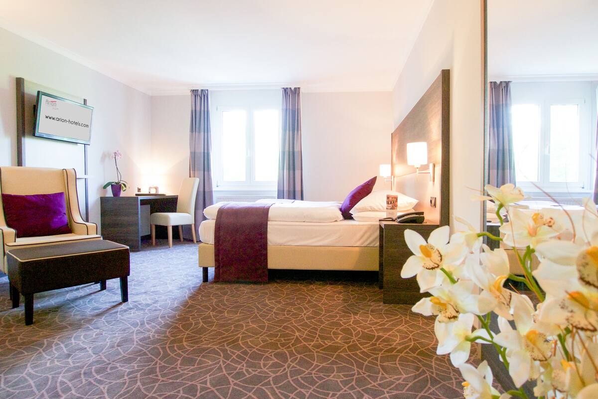 Ein Hotelzimmer mit Bett, Stuhl, Schreibtisch, Nachttisch und Spiegel.
