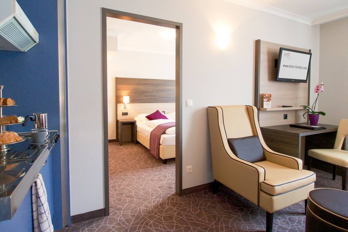Ein Hotelzimmer mit Bett, Schreibtisch, Stuhl, Fernseher und einem durchgegangenen Tür erkennbaren Badezimmer.