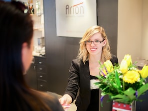 A person in a black blazer standing in front of a counter with a sign that reads "Arion". - 24hours Apartment Hotel (Vienna)