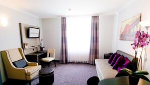 A hotel room with a sofa, armchair, dining table, and a TV on the wall. - 24hours Apartment Hotel (Vienna)