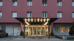 A hotel entrance with a covered entrance, glass doors, and a parking area. - 24hours Apartment Hotel (Vienna)