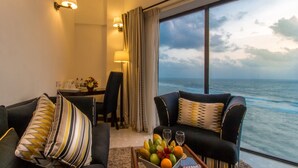 A hotel room with a large window offering a view of the ocean, a dining area with a table set for two, and a seating area with a coffee table. - The Ocean Colombo (Colombo)