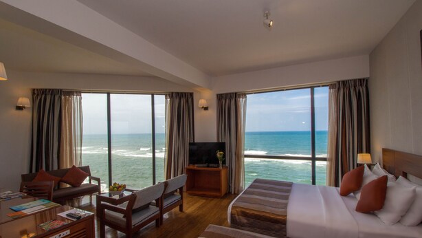 A hotel room with a large bed, a sofa, a desk with a computer, and a TV. The room has large windows with ocean views. - The Ocean Colombo (Colombo)