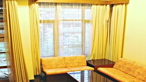 A living room with two sofas, a coffee table, and a large window with curtains. - De Orange Pasteur Guest House by HouseinBandung (Bandung)