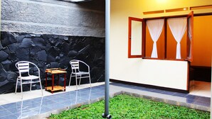 A patio with two chairs and a small table, a stone wall, and a room with a window and curtains. - De Orange Pasteur Guest House by HouseinBandung (Bandung)