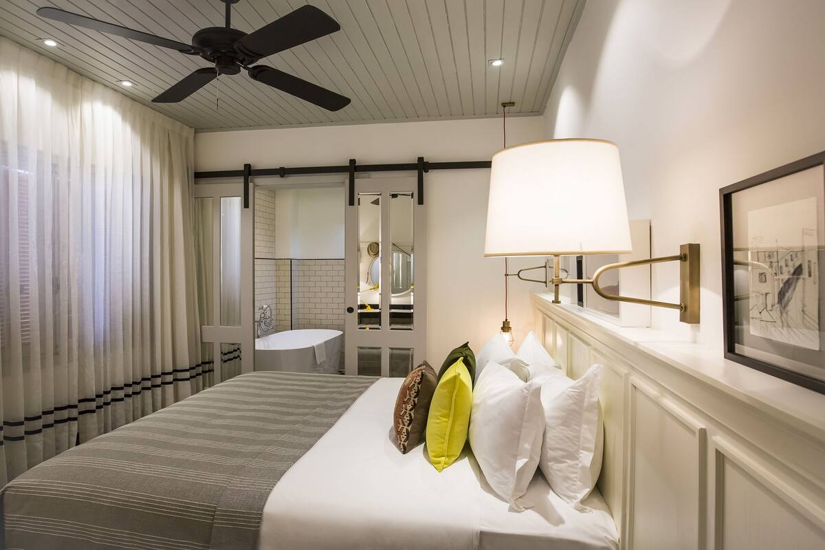 Une chambre d’hôtel comprenant un lit, une table de chevet, un miroir, une lampe fixée au mur et un tableau encadré.