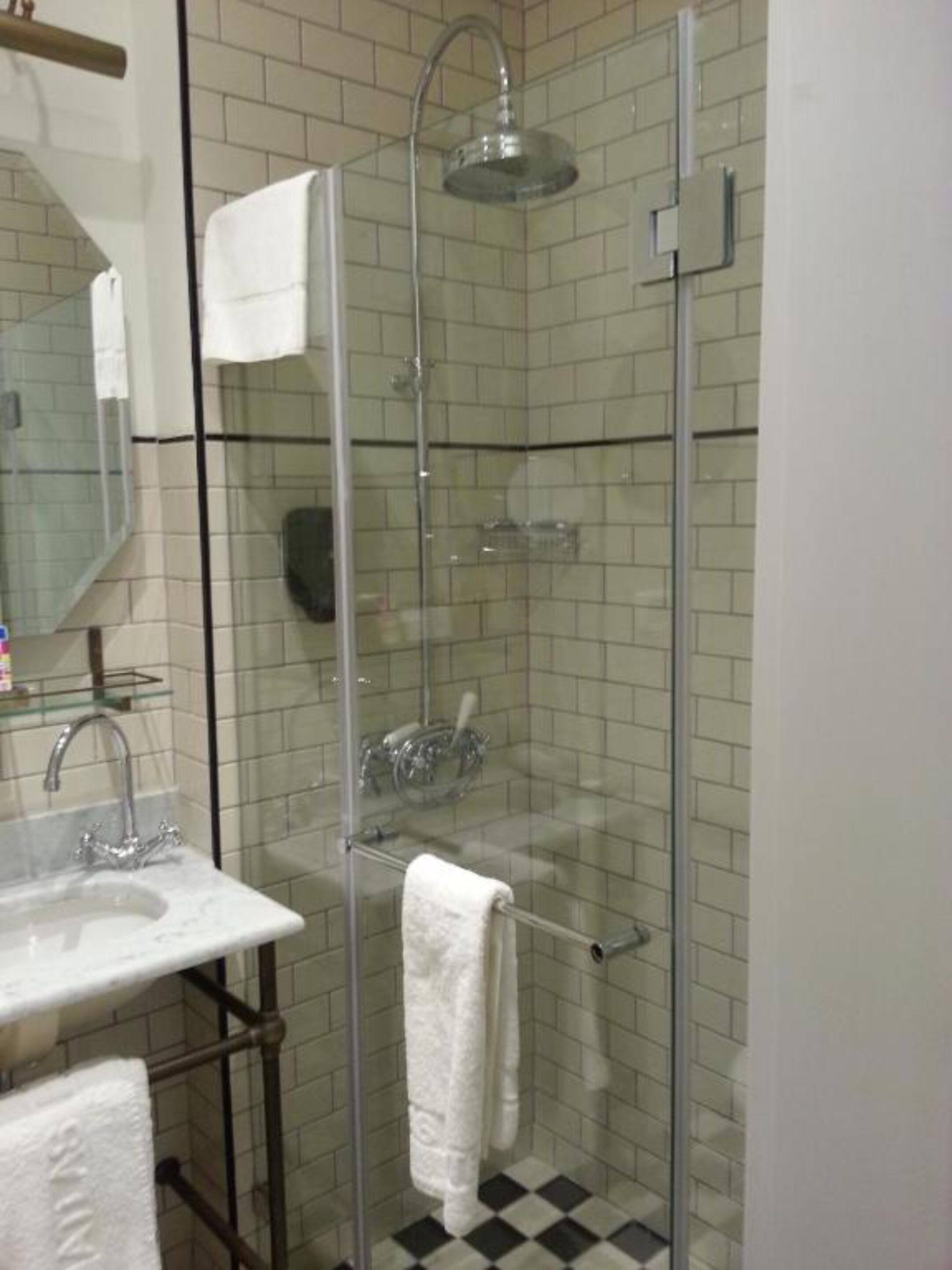 A bathroom with a glass-enclosed shower, a sink with a mirror, and a tiled floor.
