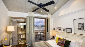 A hotel room with a bed, a desk, a chair, a table with chairs, a balcony with a view of the city, and a ceiling fan. - Market House - An Atlas Boutique Hotel (Tel Aviv)