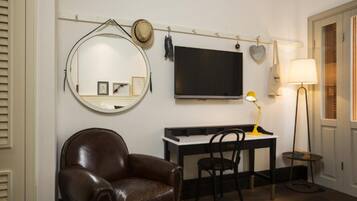 Een kamer met een bruine leren fauteuil, een bureau met een computer, een televisie, een lamp en een tafeltje met boeken.