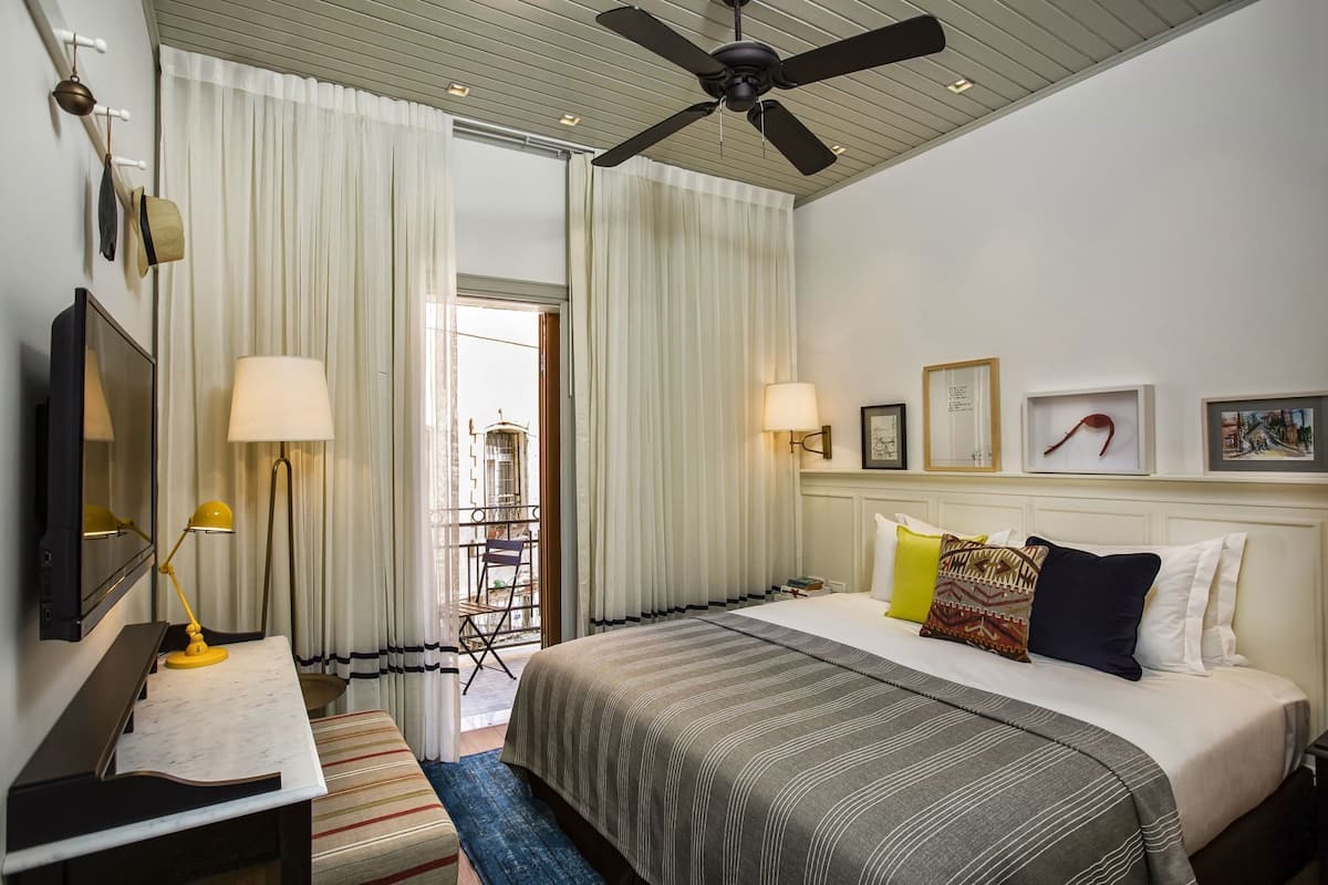 Une chambre d’hôtel avec un lit, des lampes de chevet, un ventilateur de plafond, une télévision et un balcon avec vue.