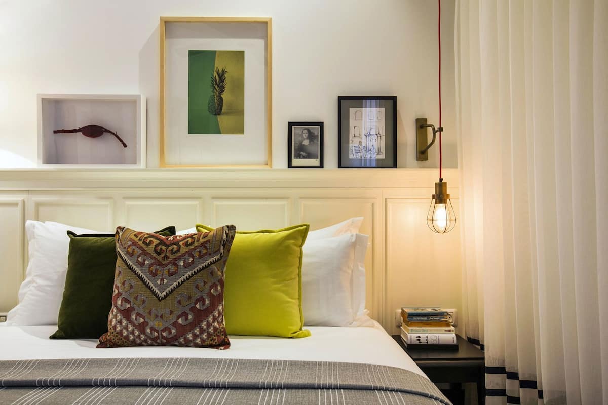 Un lit bien fait, agrémenté d’oreillers à motifs, une œuvre d’art représentant un ananas, encadrée, et une esquisse architecturale encadrée accrochée au mur.