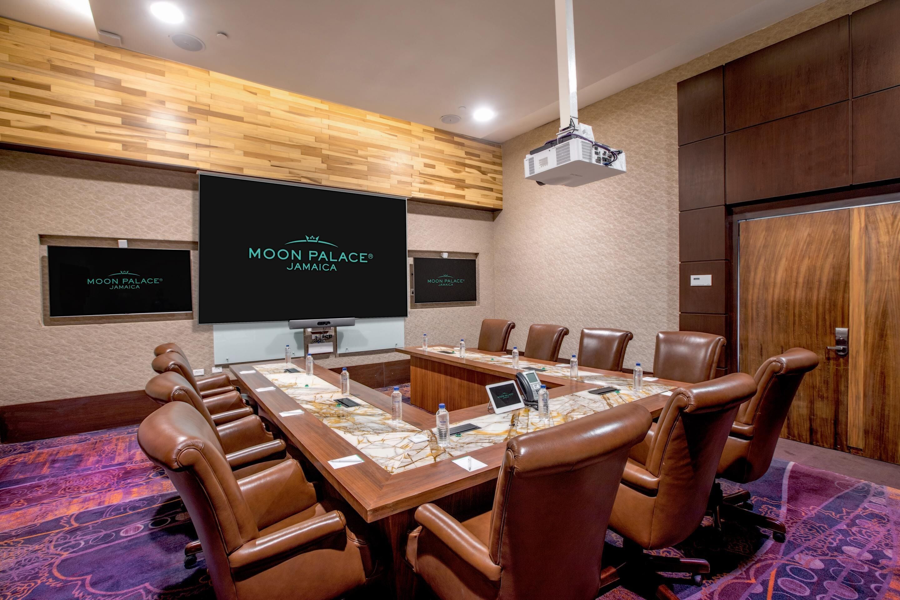 A conference room with a long table, leather chairs, a projector, and a screen displaying "Moon Palace Jamaica".