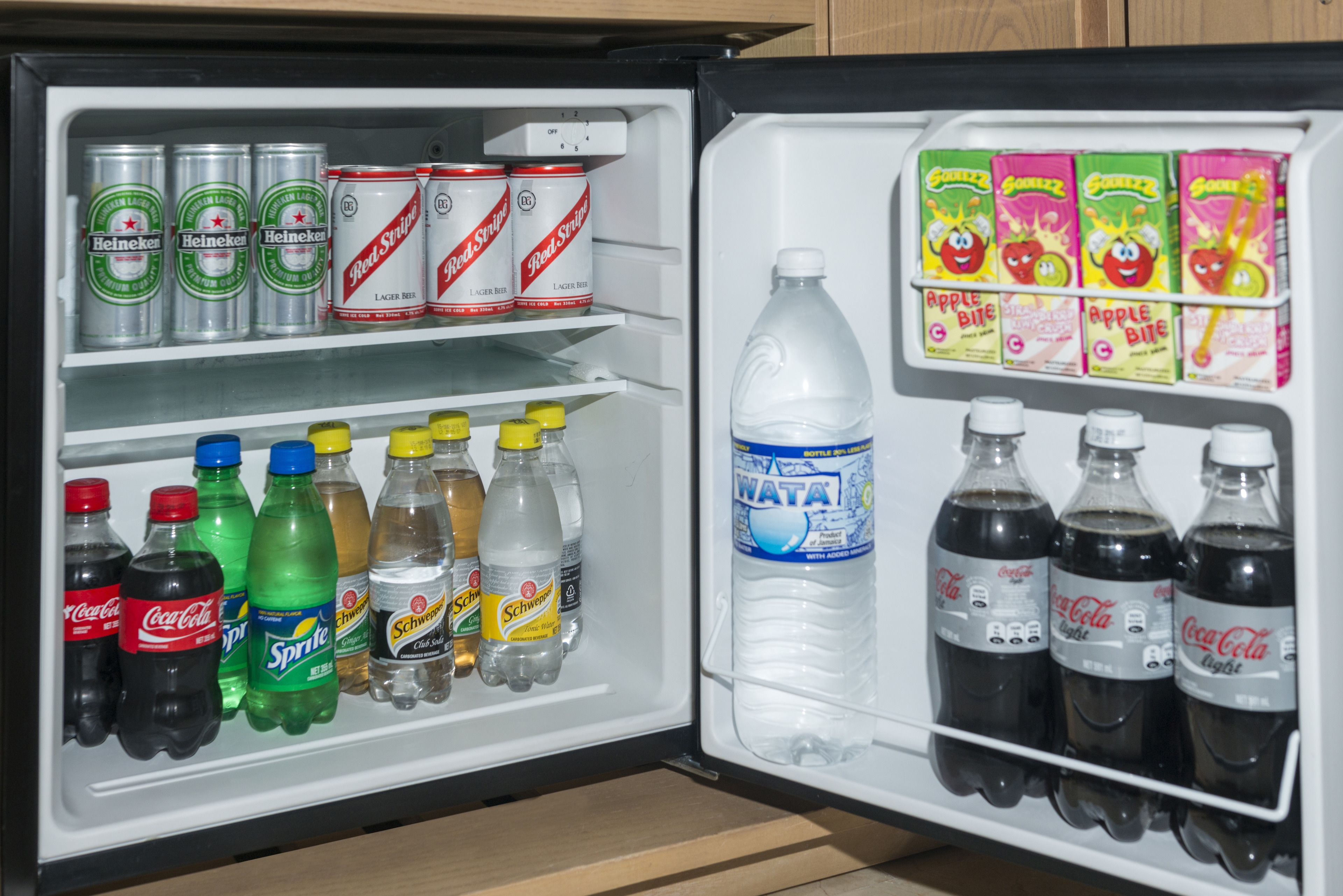 Un frigorifero pieno di diverse bevande, tra cui Heineken, Red Stripe, Sprite, Coca-Cola e Wata.