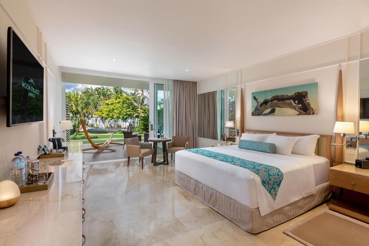 A modern hotel room with a large bed, a desk, a chair, and a view of the outdoors.