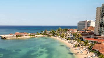 Un resort costero con playa, palmeras y un gran edificio de hotel.