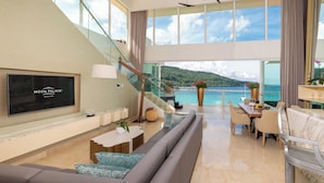 A spacious living area with a large TV, comfortable seating, a dining table, and a view of the sea.
