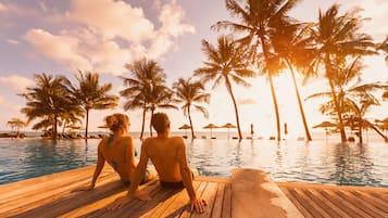 Couples can enjoy a romantic view from this deck overlooking a pool surrounded by palm trees and lounge chairs.