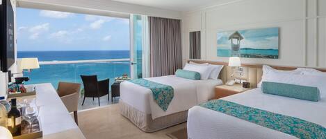 A hotel room with two beds, a desk, and a view of the ocean.