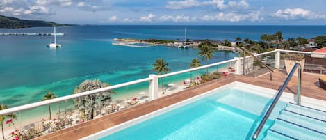 Una piscina con vista al océano, un barco y una playa con palmeras.