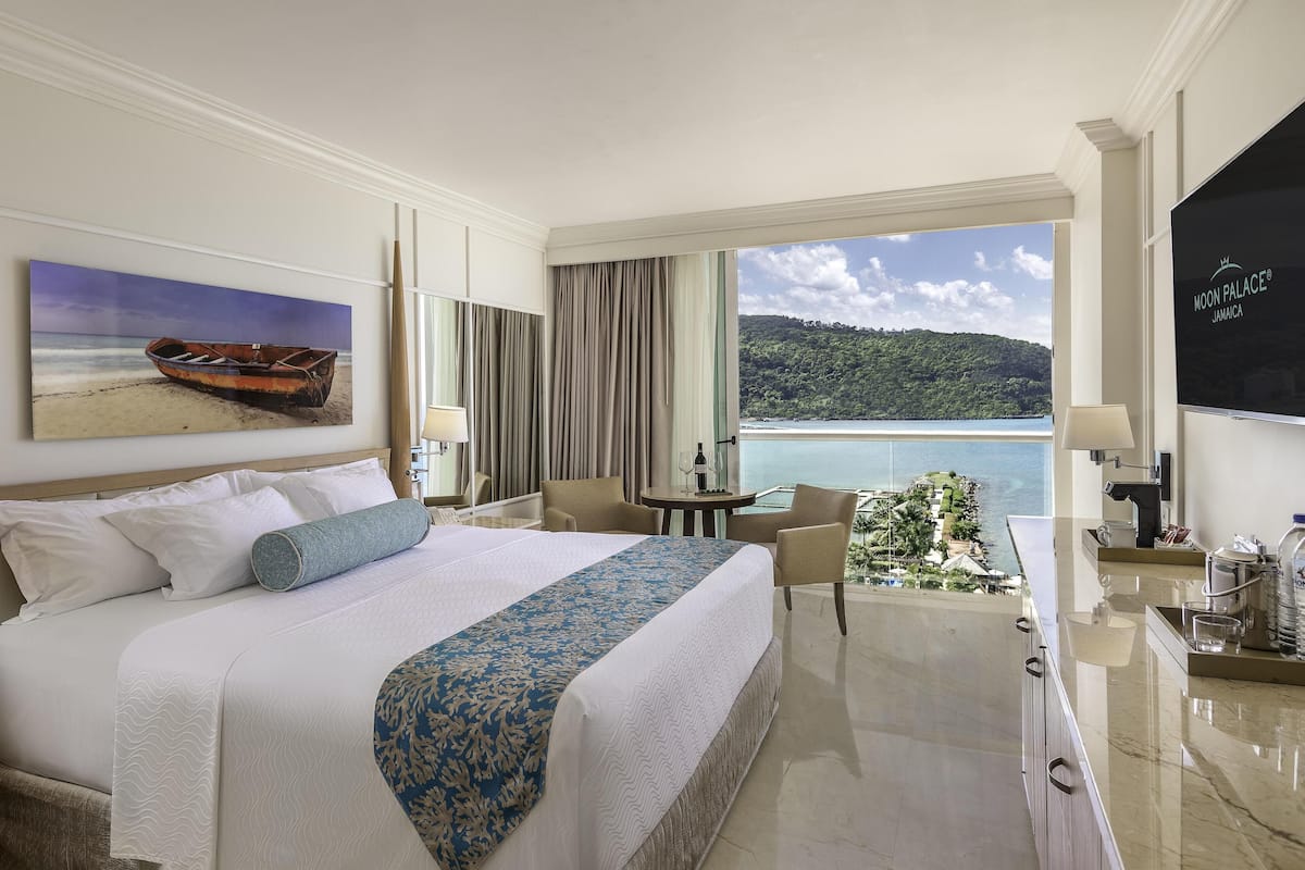 A hotel room with a large bed, a desk, a chair, and a view of the ocean.