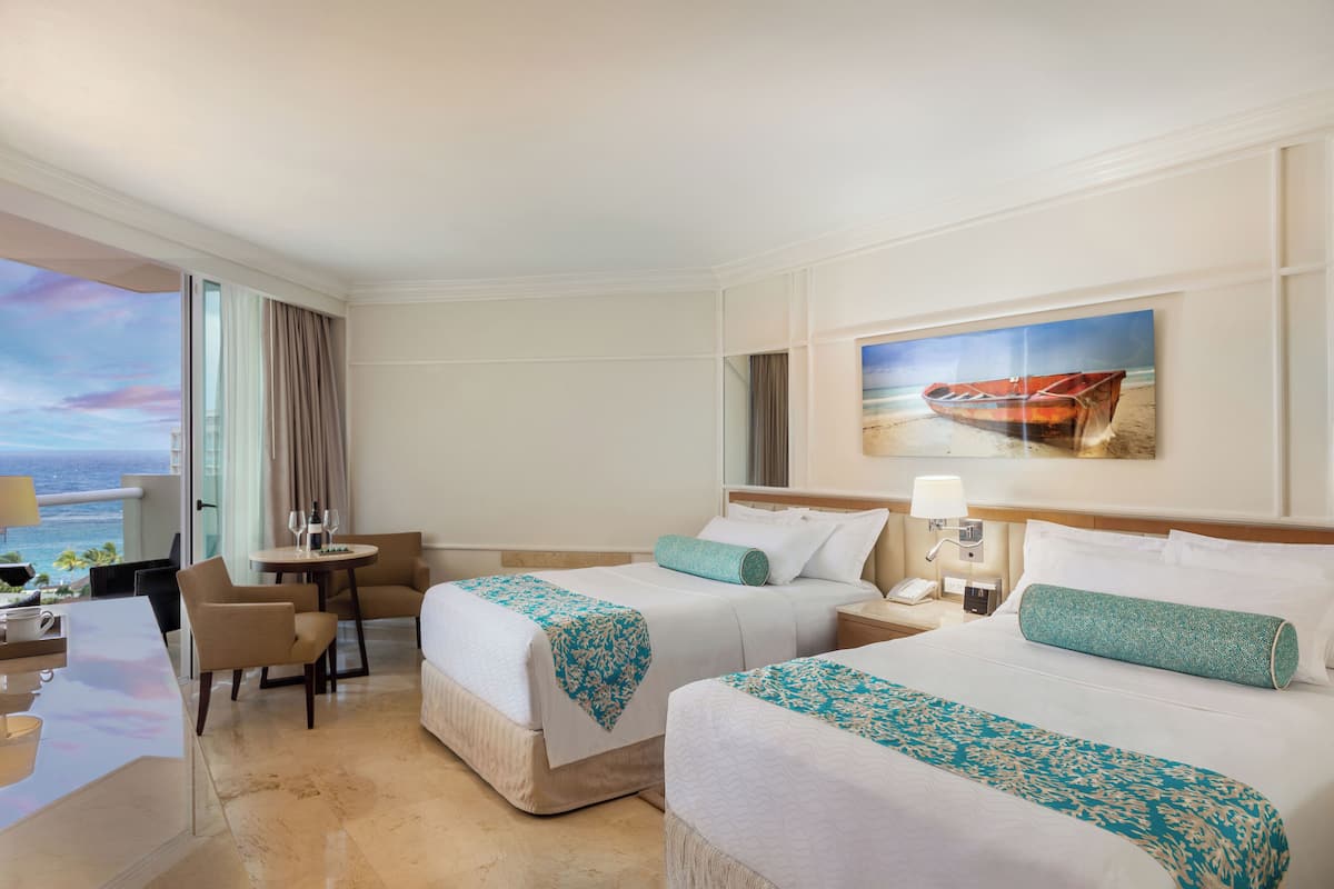 A hotel room with two beds, a desk, a chair, a small table, and a painting of a boat on the wall.