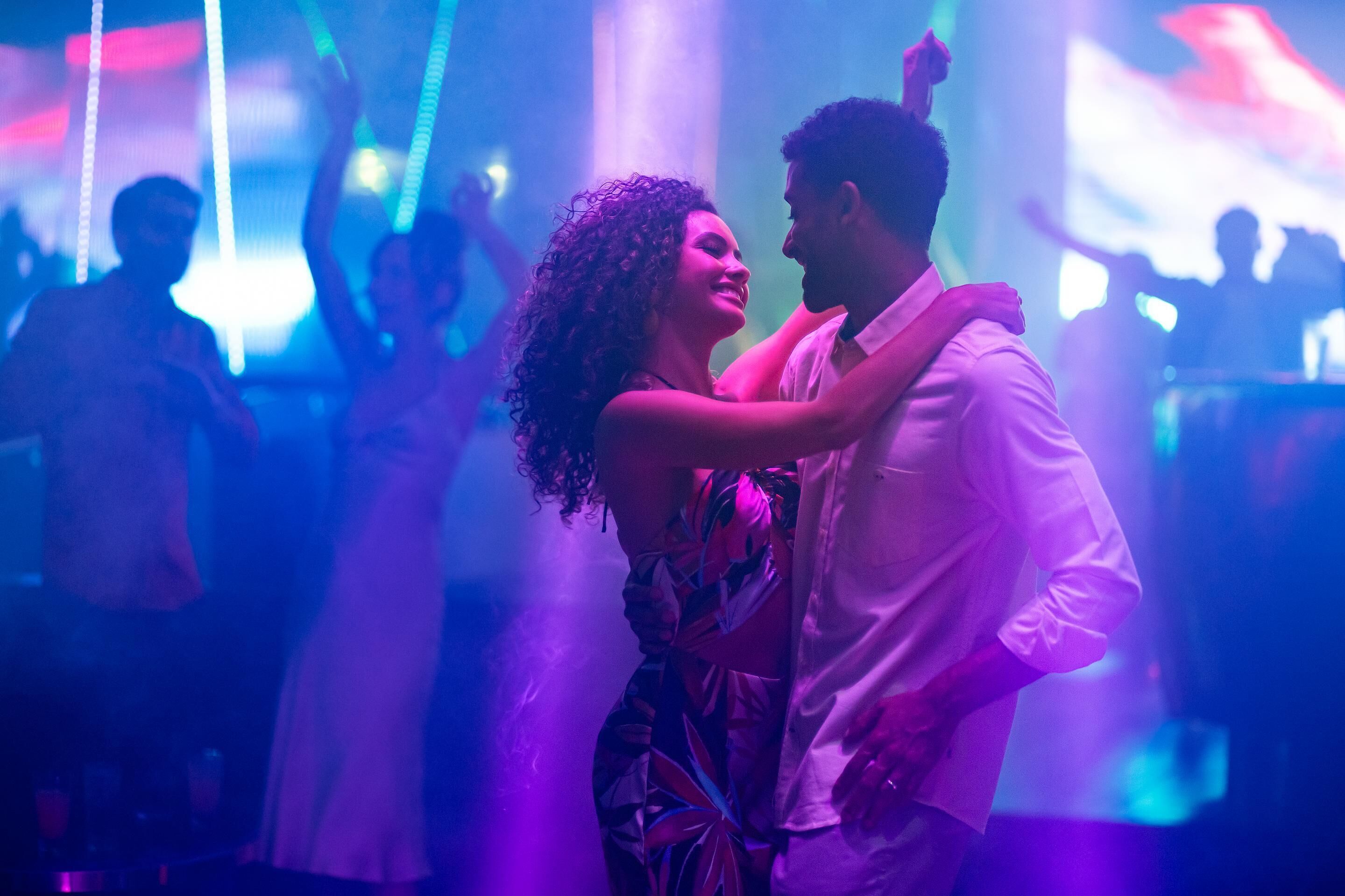 Una pareja bailando en un club nocturno, con gente en el fondo.