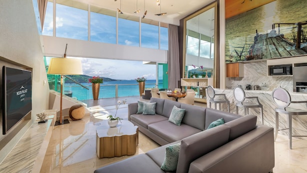A modern living room with a large sofa, a coffee table, and a TV. There is a balcony with a view of the sea. - Moon Palace Jamaica – All Inclusive (Ocho Rios)