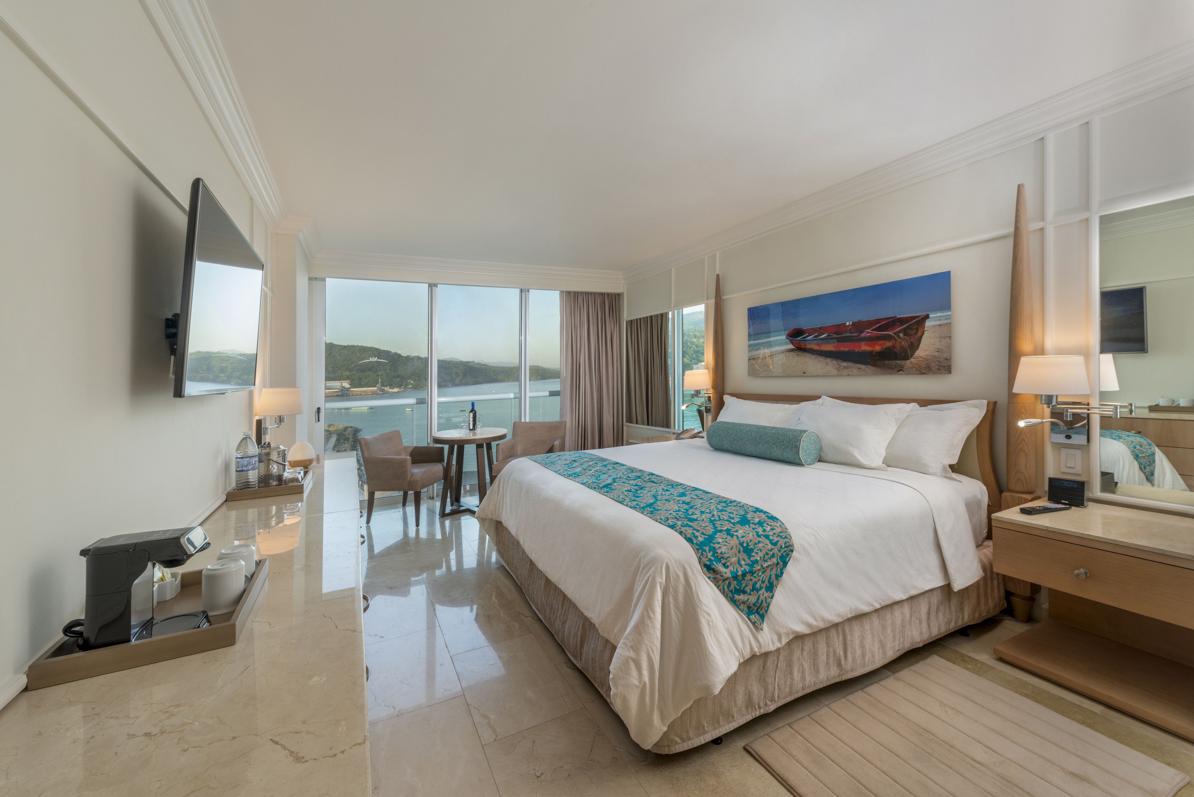 Quarto de hotel com uma cama grande, uma escrivaninha, uma cadeira, uma televisão e um quadro de um barco na parede.