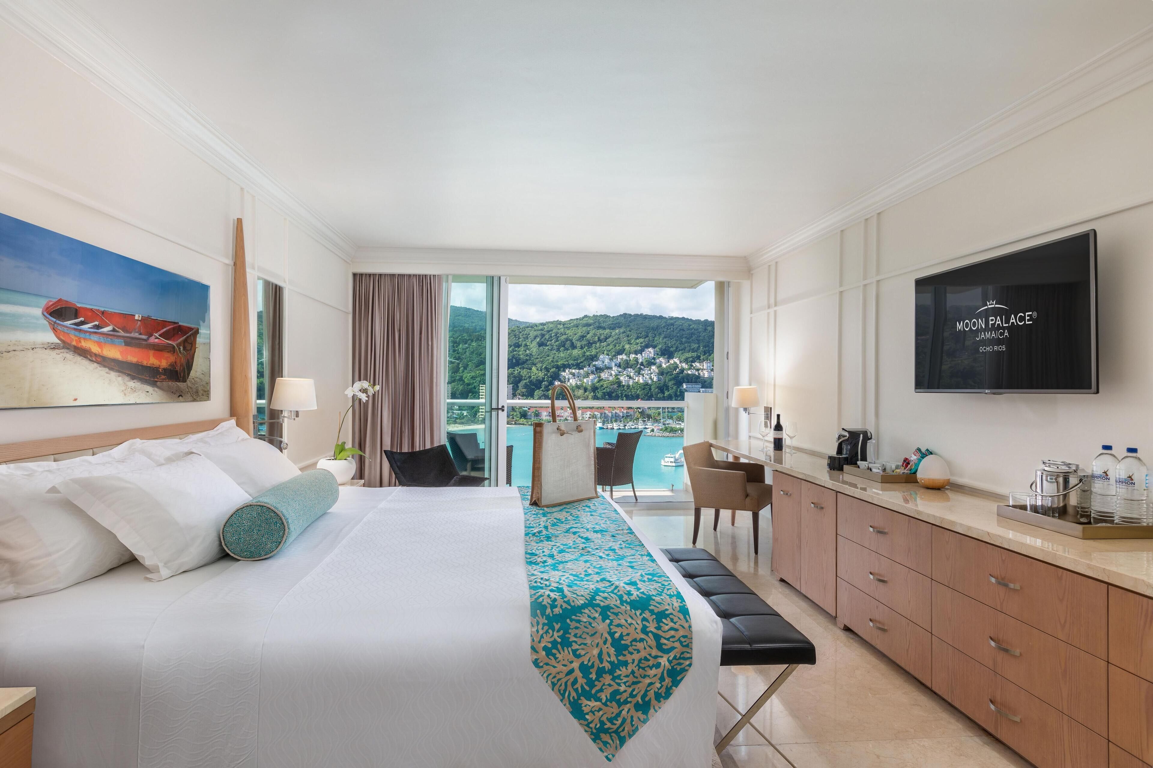 Une chambre d’hôtel avec un lit, un bureau, une chaise, une télévision et une vue sur la mer.