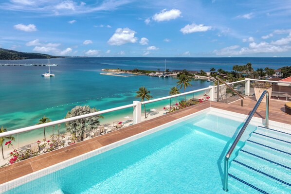 Una piscina con vista al océano, un barco y una playa con palmeras.