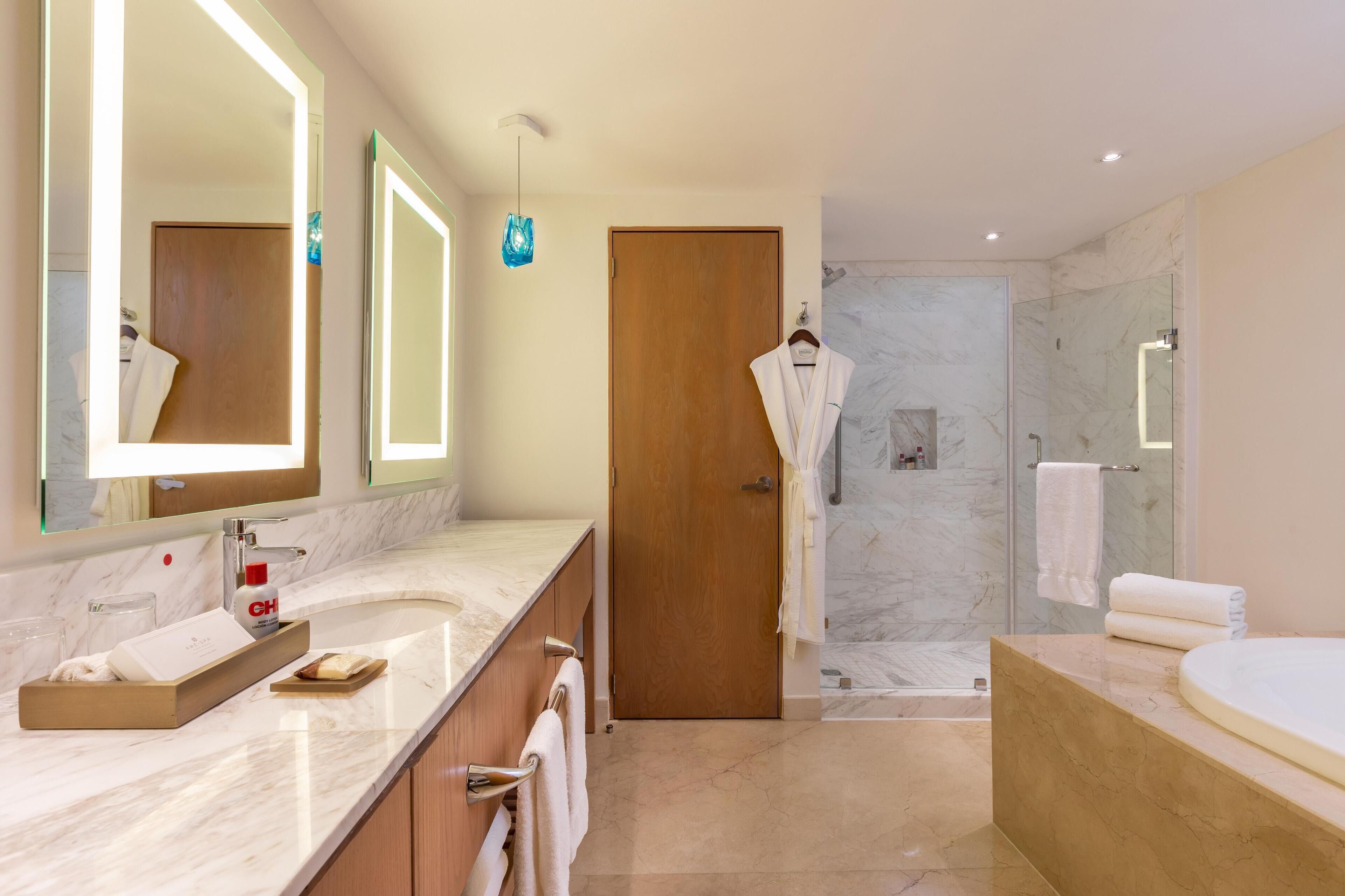 A modern bathroom with a marble countertop, a large mirror, a wooden door, a glass shower enclosure, and a bathtub.