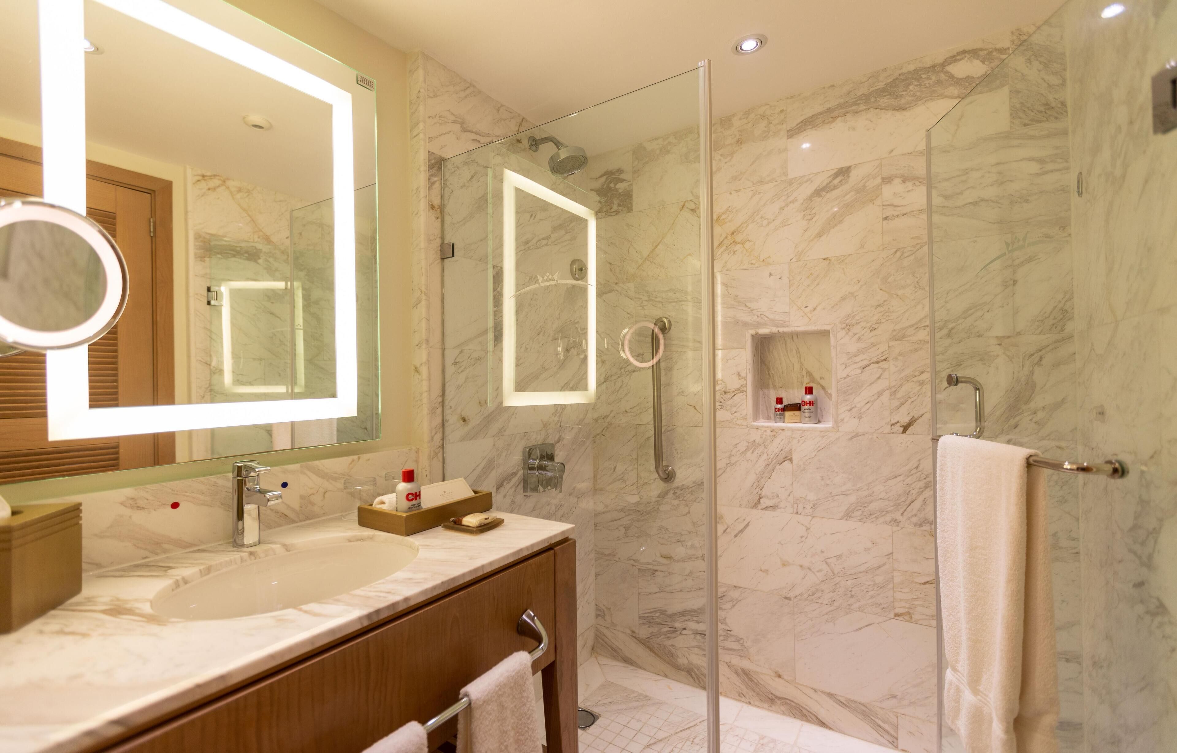 Een moderne badkamer met een douchecabine van glas, marmeren wanden, een grote spiegel en een wastafelmeubel met een wastafel en handdoekhouder.