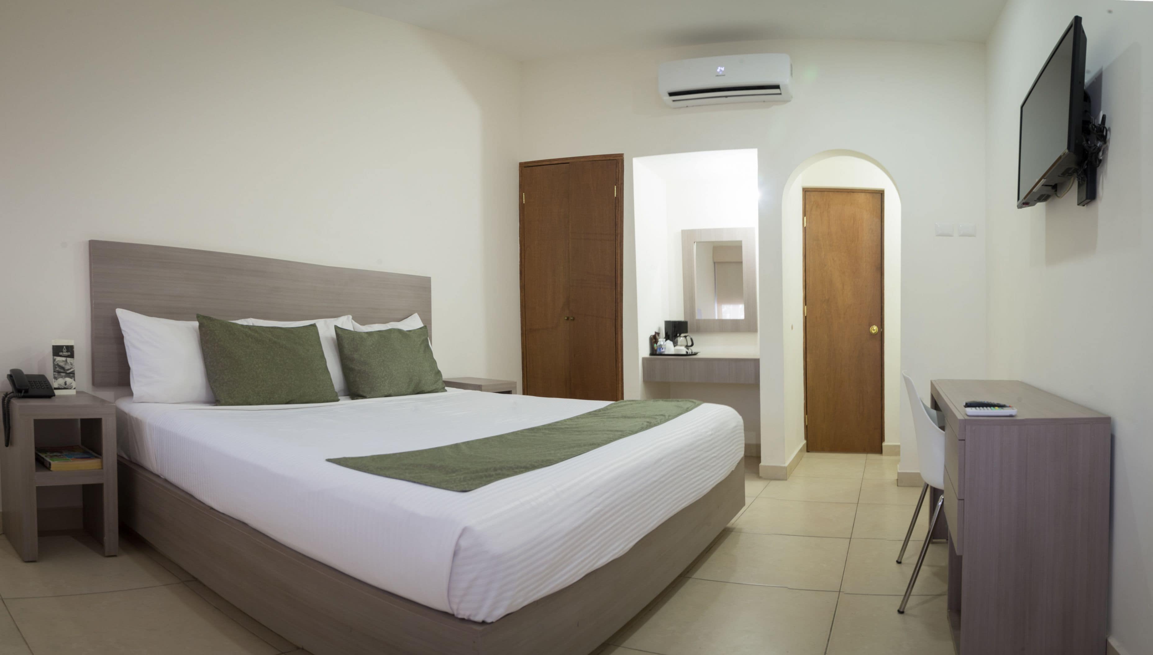 Una habitación de hotel con una cama grande, una mesita de noche, un escritorio, una silla, un equipo de aire acondicionado y un televisor fijado a la pared.