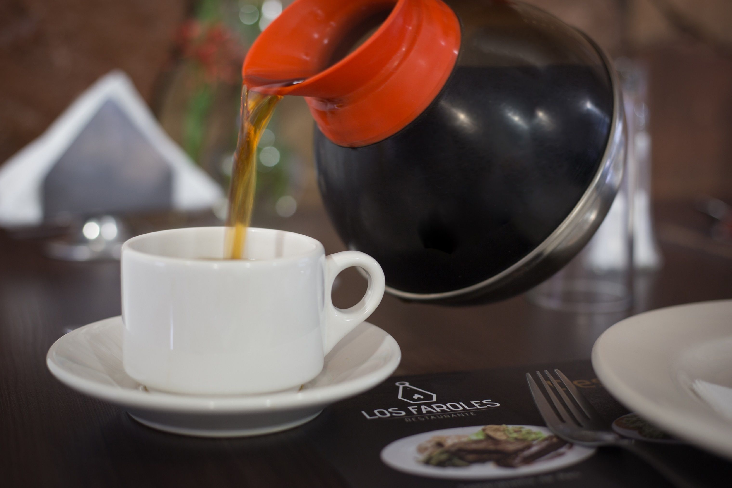 Café sendo servido de uma chaleira vermelha para uma xícara branca em um pires.