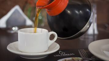 Kaffee wird aus einer roten Kanne in eine weiße Tasse auf einem Untertasse gegossen.