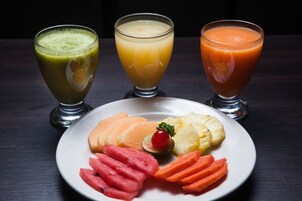 Tres vasos de jugo y un plato con frutas y verduras cortadas.