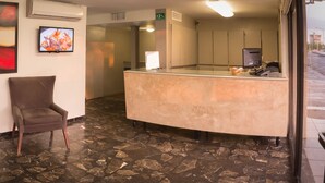 A reception area with a marble floor, two brown chairs, a reception desk, a TV, and a large abstract painting on the wall. - Hotel La Riviera (Culiacán)