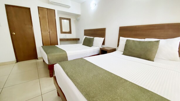 A hotel room with two single beds, a double bed, a wooden headboard, a nightstand, a mirror, and an air conditioning unit. - Hotel La Riviera (Culiacán)