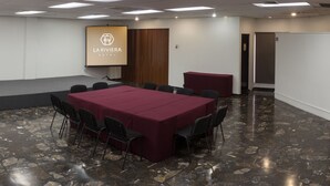 A conference room with a marble floor, a large table with chairs, a whiteboard, and a screen displaying 'LA RIVIERA HOTEL'. - Hotel La Riviera (Culiacán)