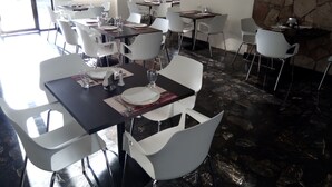 A restaurant with white chairs and tables, stone walls, and large windows. - Hotel La Riviera (Culiacán)
